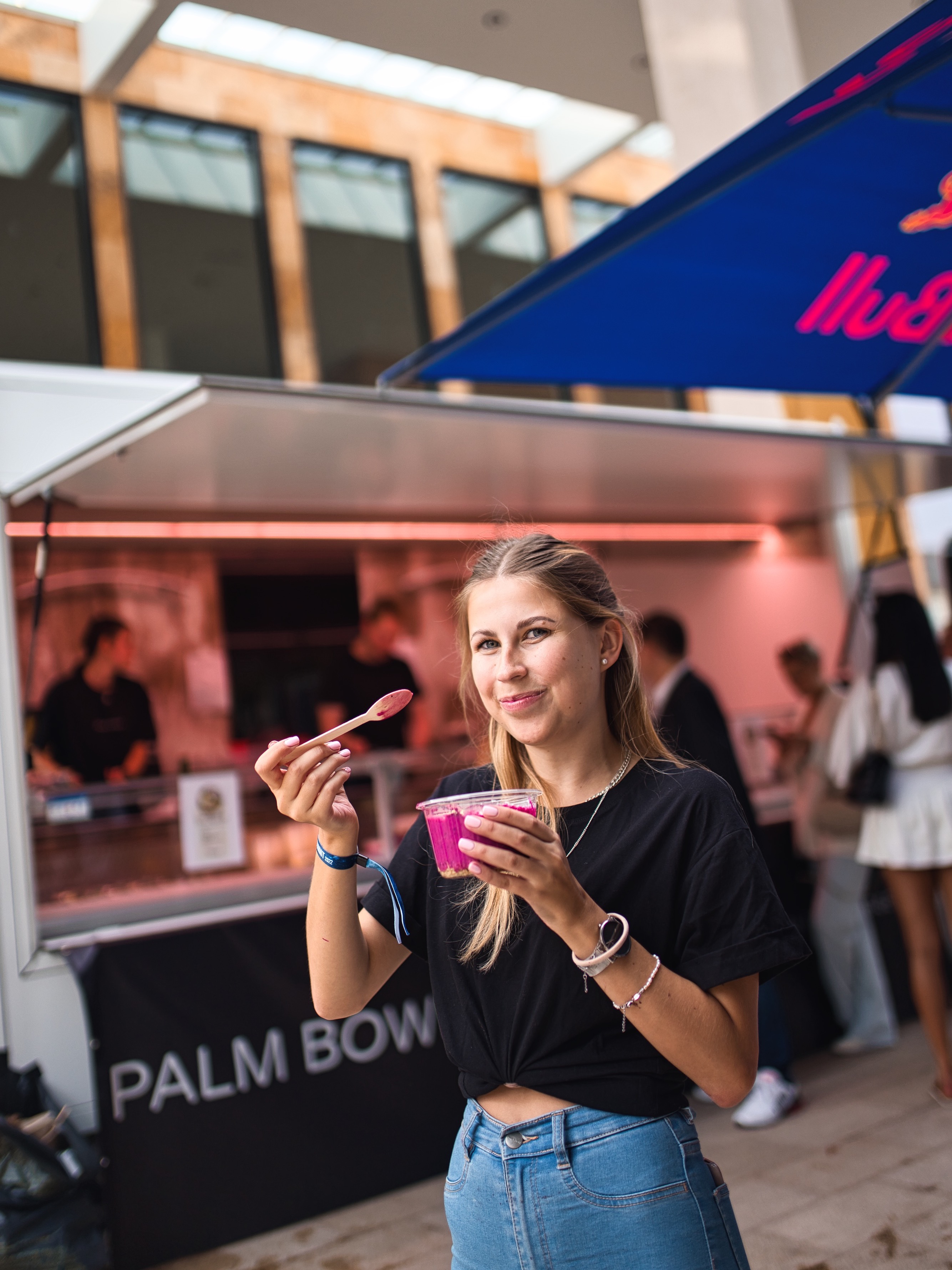 Frau isst Smoothie Bowl vor einem Foodtruck mit der Aufschrift Palm Bowls