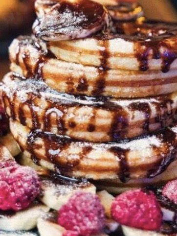 Nachspeise eines Caterings in Form von Pancakes mit Schokoladensauce, Himbeeren und Puderzucker